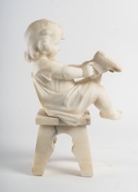 Statue en albâtre représentant une petite fille assise sur un tabouret et jouant avec des chaussures .