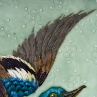 Plat en céramique émaillée à décor polychrome représentant un canard colvert en plein vol au dessus d’un étang, entouré de fleurs