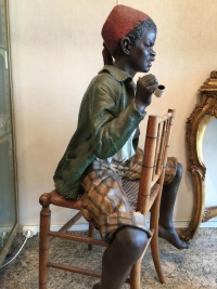 Enfant noir en terre cuite sur une chaise en bambou et cannage. Réf: 356