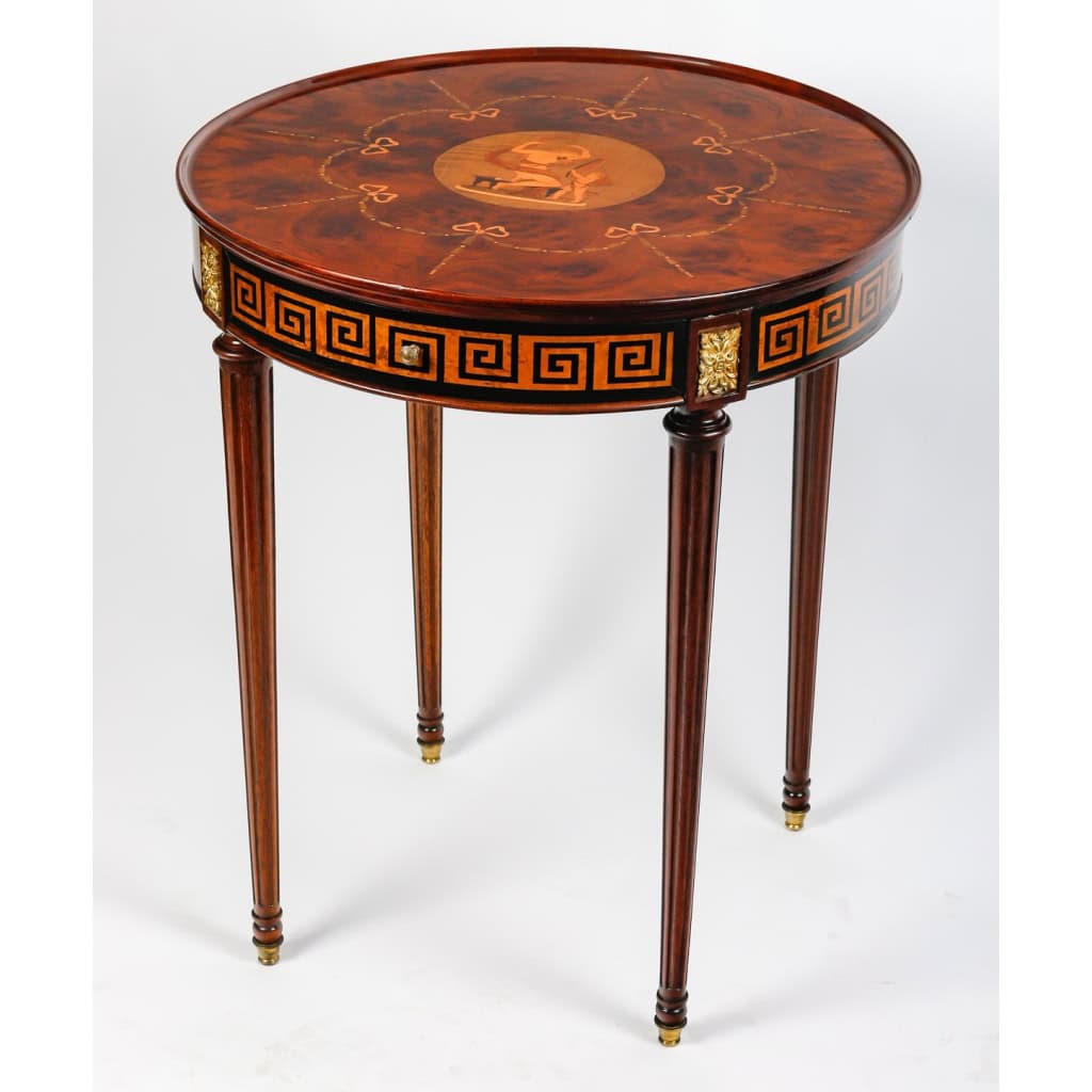 Table ronde ouvrant par un tiroir en marqueterie de bois précieux. Plateau finement marqueté d’une scène d’après l’Antique | Biron ||||||||