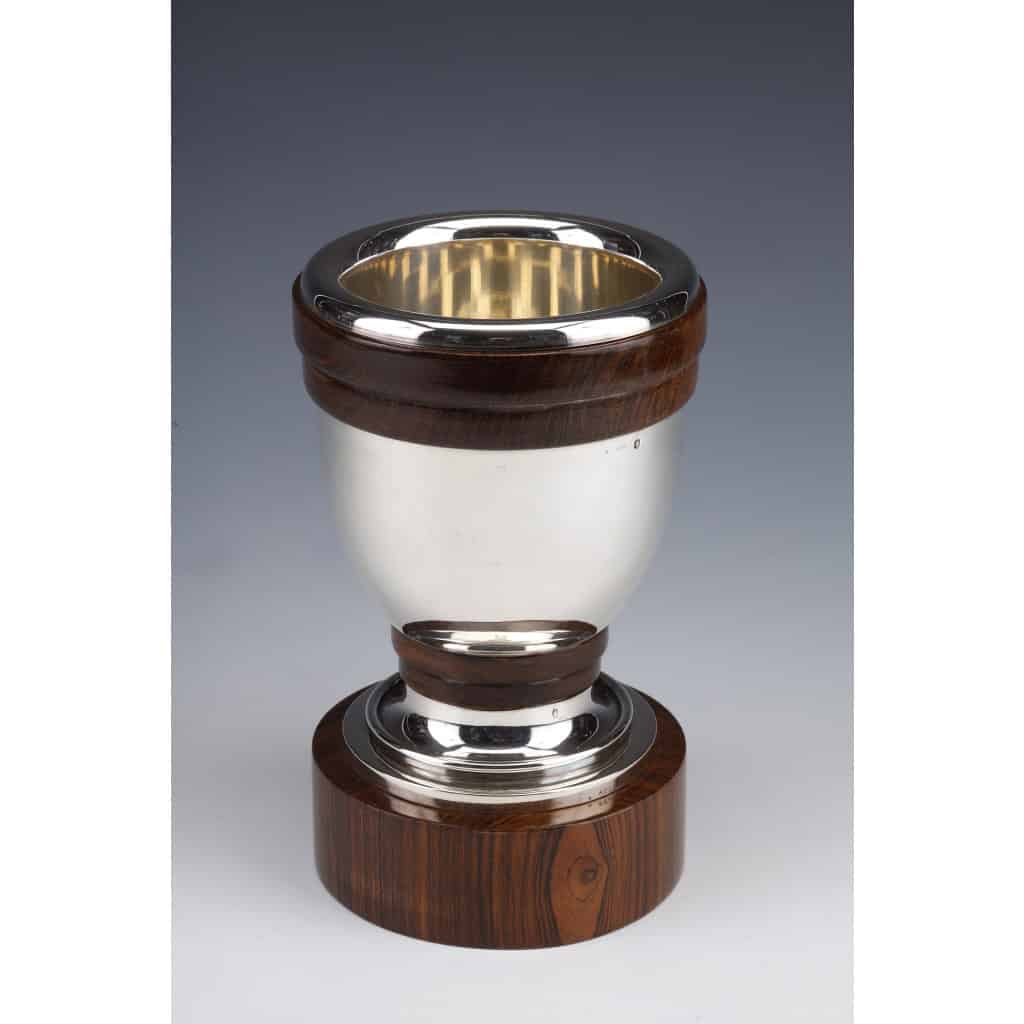 Gustave KELLER – Vase en argent massif époque ART DECO | Biron Gustave KELLER - Vase en argent massif époque ART DECO VASE en argent massif de forme ovoïde moderniste, monté sur un socle en palissandre, le piédouche et le col sont cernés par un double anneau en palissandre. Dimensions : hauteur 20,5 cm - diamètre de la base 12 cm - diamètre du col 13 cm Matière : Argent 1er titre 950/°°° Poids : 1220 grammes brut Poinçon : MINERVE Epoque : ART DECO vers 1930 Orfèvre : Gustave KELLER Origine : France / PARIS