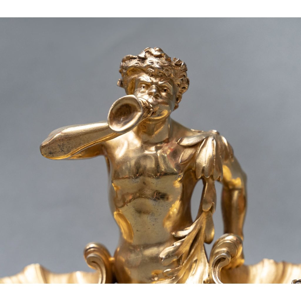 Maison BOUDET – Exceptionnelle Paire de salerons en vermeil 19e siècle | Biron Maison BOUDET - Exceptionnelle Paire de salerons en vermeil XIXe Exceptionnelle paire de salerons en vermeil représentée par un triton soufflant dans une conque, au milieu de deux grands coquillages posés sur une base ovale à contours feuillagés. Ici le thème marin s'inspire du bassin "Neptune" de Versailles et d'un centre de table exécuté par Emile Froment Meurice pour le duc Medina Celi, aujourd'hui conservé au Palais royal de Madrid. On peut attribuer ce travail à la maison Boudet, 43 boulevard des Capucines à Paris. Exemple cette Importante paire de rafraichissoirs et leurs présentoirs adhérents en argent et vermeil. Epoque fin du XIXe siècle exécutée par la maison BOUDET. (photo jointe) Dimensions : longueur 24 cm - largeur 13,4 cm - hauteur 16,5 cm Matière : Argent vermeil 1er titre 950/°°° Poids : 2.900 grammes Poinçons : MINERVE et SANGLIER Epoque : XIXè siècle Orfèvre : Attribué à Victor BOUDE losange avec trace d'initial d'orfèvre Origine : France/Paris Victor Boudet est un orfèvre ciseleur qui a insculpé son poinçon en 1894. Son atelier situé 43 Boulevard des Capucines est encore en activité en 1902 avant son déménagement. Ces magnifiques salerons ne semblent pas présenter de poinçon d'orfèvre. Il est donc vraisemblable que Boudet ait ciselé cette pièce avec une grande virtuosité mais il est impossible d'assurer qu'il en soit l'orfèvre.