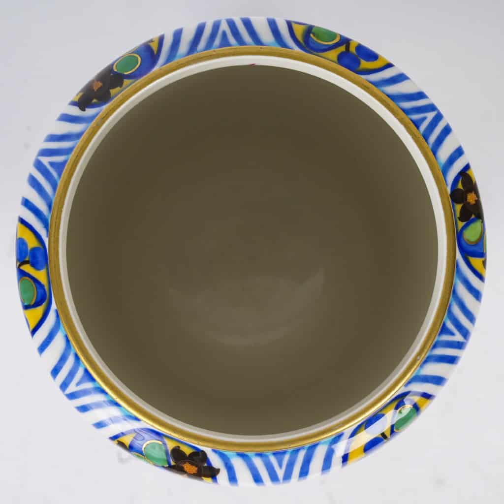 Très élégant vase en porcelaine blanche à décor abstrait végétalisant géométriques dans les tons de bleu, vert, noir, jaune et rouge. Pièce signée, au cachet de la Manufacture National de Sèvres, décor peint d’après l’artiste Jane Levy, travail de 1925. | Biron 