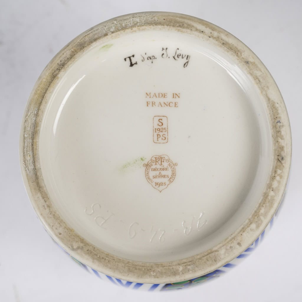 Très élégant vase en porcelaine blanche à décor abstrait végétalisant géométriques dans les tons de bleu, vert, noir, jaune et rouge. Pièce signée, au cachet de la Manufacture National de Sèvres, décor peint d’après l’artiste Jane Levy, travail de 1925. | Biron 