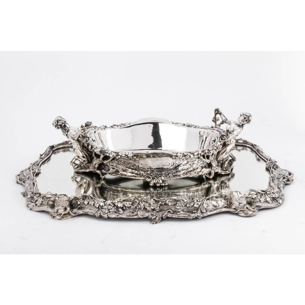 ORFEVRE C.CHRISTOFLE Silver-plated bronze centerpiece called “The Forest” XIX19th century | Biron Silver-plated bronze centerpiece called "The Forest" by C. CHRISTOFLE XIXth century Table centerpiece in silver-plated bronze composed of an oval tray with a mirror base mounted on an oak parquet floor and set with a silver-plated bronze ingot mold with a plant decoration of tree branches, in the center is placed a magnificent planter with the same forest decoration whose handles are represented by two young fauns. This piece was entitled "LA FORÊT". Dimensions: Tray Length 0 cm - width 70 cm - Height 46 cm Planter: length 6 cm - width 48 cm - height 24 cm Material: Bronze Hallmarks: CHRISTOFLE in full CC balance and three stars in a square Order number: 14 and 2365582 Period: Mid-222657th century XIX10th century Goldsmith: CHARLES CHRISTOFLE