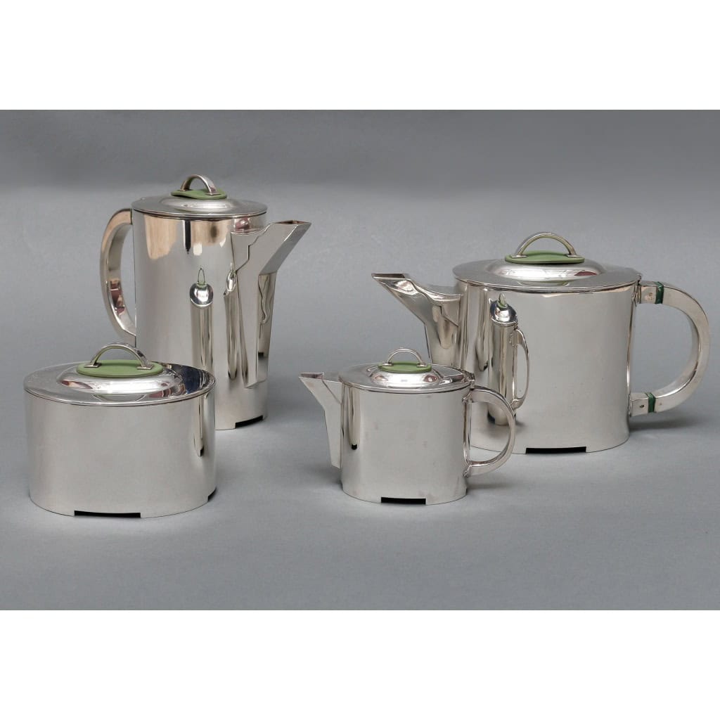 ORFEVRE C. FJERDINGSTAD – Service thé/café moderniste en argent massif Circa 1950 | Biron C. FJERDINGSTAD - Service thé/café moderniste en argent massif Circa 1950 Service thé/café en argent massif moderniste de forme ovale composé d’une théière, une cafetière, un pot à lait et un sucrier. Chaque pièce possède un couvercle dont la prise est fixée sur une plaque ovale en résine. Légère fissure sur une plaque de résine. Dimensions : théière : 21 cm x 9 cm hauteur 12 cm- Cafetière 19 cm x 7,5 cm hauteur 16 cm sucrier 10,5 cm x 8,5 cm hauteur 8,5 cm – Pot à lait 12 cmx6 cm hauteur 8,5 cm Matière : Argent 1er titre 950/°°° Poids : 1616 grammes Poinçon : MINERVE – N°065 Orfèvre : CHRISTIAN FJERDINGSTAD (1891-1968) Origine : France/Paris CHRISTIAN FJERDINGSTAD (1891-1968) Christian Fjerdingstad est un orfèvre hors du commun, d'origine danoise et française de cœur . Son œuvre artistique est à part empreinte de ces deux influences. Il a su créer un art mélangeant finesse et modernité renouvelant ainsi le langage stylistique de l'orfèvrerie. Christian Fjerdingstad représente sans conteste le trait d'union entre Puiforcat et Jensen par les caractéristiques de son œuvre. S'inspirant des pièces mécaniques dans la forme ou dans le détail, il tempérerait cette modernité par des touches de poésie. Ainsi, il employait des matières minérales ou synthétiques dans des éléments d'ornementation, tel que l'ambre, de l'ivoire ou de la corne qui faisait référence à la nature qu'il admirait tant.