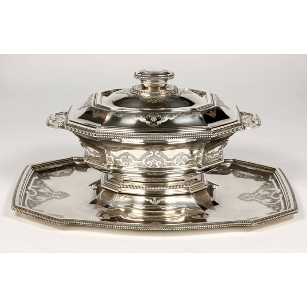 Orfèvre ROUSSEL - Centre de table sur son dormant en argent, XIXè Centre de table en argent massif composé d'une importante soupière couverte montée sur pièdouche et enchassée dans son plateau, forme octogonale, l'ensemble est bordé de godrons et gravé d'un décor à la Bérain dans le style Régence. Dimensions : longueur 52,5 cm - largeur 32,5 cm Matière : argent 1er titre 950/°°° Poids : 7600 grammes Poinçon ; MINERVE Epoque : XIXè siècle NAPOLEON III Orfèvre : D. ROUSSEL à PARIS Origine : FRANCE/PARIS
