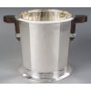 PUIFORCAT – Seau à Champagne « Bayonne » en argent massif ART DECO | Biron PUIFORCAT – Seau à Champagne "Bayonne"en argent massif ART DECO Important Seau à Champagne en argent massif, à décor de deux sections de pans coupés, séparées par des arrondis sur lesquels sont fixées les anses en bois de forme géométrique et renforcées par des joncs filetés en argent. au modèle Bayonne . Le corps uni est cintré d’un bandeau cerclé des trois joncs à la base. Dimensions : Hauteur 21,5 cm – Largeur au col 21,5 cm Largeur aux anses 29,5 cm Matière : Argent 1er titre 950/°°° Poids : 2 715 grammes Poinçon : MIINERVE Epoque : Puiforcat Paris – Edition 1985 d’après un modèle créé en 1935 par Jean Elysée Puiforcat (1897-1945) Orfèvre : JEAN E. PUIFORCAT à PARIS Origine : France/Paris JEAN PUIFORCAT par Françoise de Bonneville page 82 (saucière au modèle)