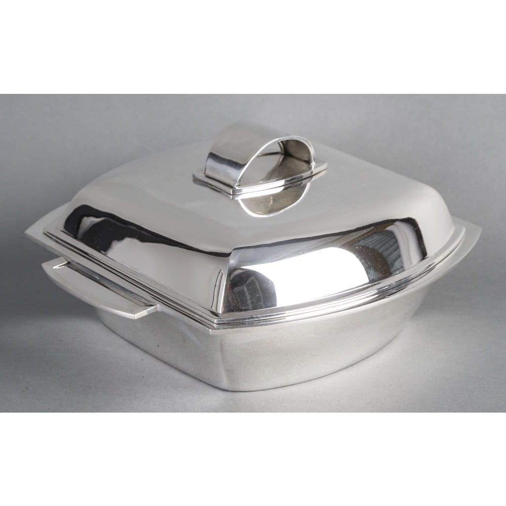 CHRISTOFLE – SOUPIERE MODERNISTE SUR SON PLATEAU EN ARGENT MASSIF ART DECO | Biron CHRISTOFLE - SOUPIERE MODERNISTE SUR SON PLATEAU EN ARGENT MASSIF ART DECO Centre de table formé d'une soupière couverte sur son plateau, de forme rectangulaire à fond plat et flanqué de deux anses latérales, le couvercle à doucine est surmonté d'une prise en demi-cercle. La soupière repose sur un plateau en argent aux mêmes formes incurvées. Dimensions : Soupière : 26 x 22 x 12 cm - base 16 x 16 cm Plateau : 30 x 30,5 cm hauteur 1,5 cm Matière : Argent 1er titre 950/°°° Poids : 2 060 grammes Poinçon : MINERVE Epoque : ART DECO vers 1930 Orfèvres : CHRISTOFLE & RAVINET D'ENFERT pour le plateau Origine : France/Paris