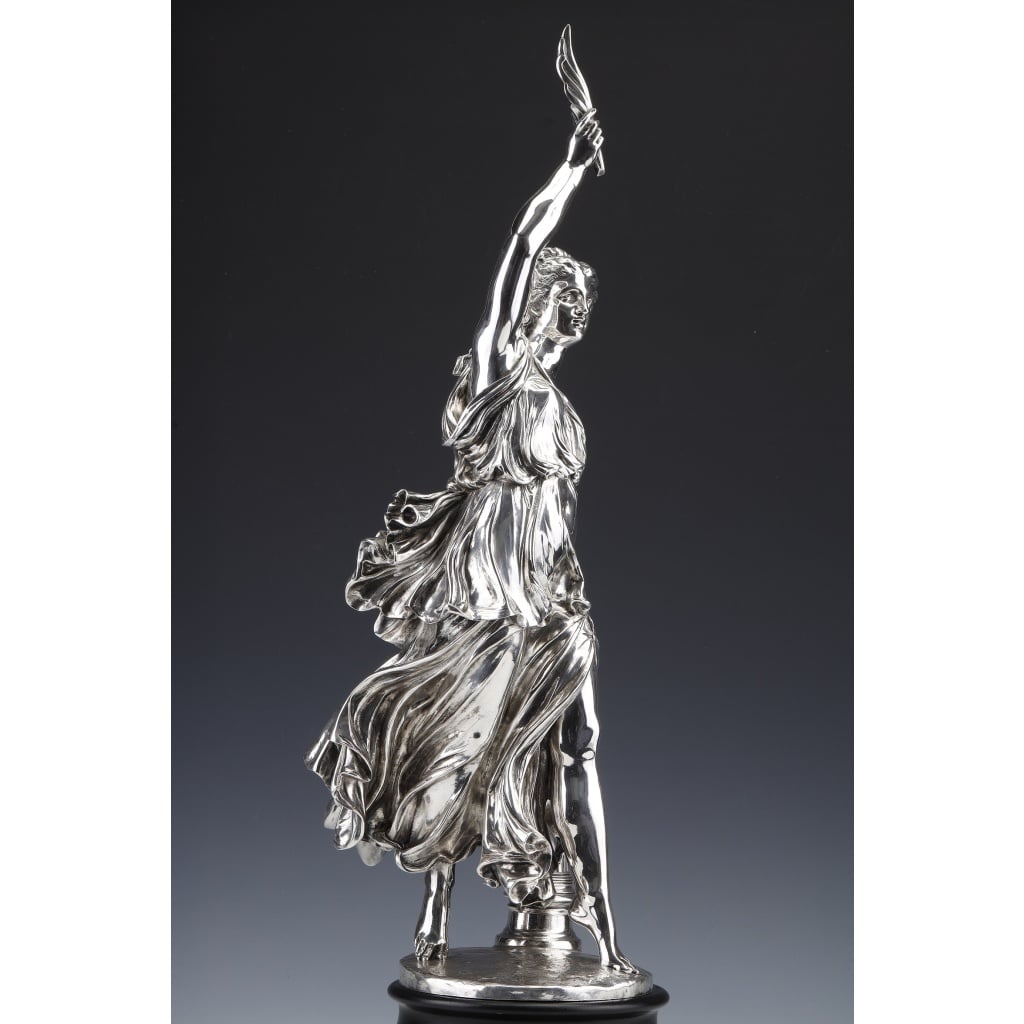 Jacques Léonard MAILLET – Statue allégorique en argent massif – XIXe | Biron Jacques Léonard MAILLET - Statue allégorique en argent massif - XIXeSTATUE ALLEGORIQUE en argent massif représentant une déesse dans une magnifique robe drapée, haletante encore de la course qu'elle vient de faire, élève au dessus de sa tête la palme qu'elle vient de remporter. Statue répertoriée dans le livre de H. BOUILHET " L'Orfèvrerie Française des 18e & 19e siècles". Cette statue a fait l'objet d'une récompense pour une victoire de l'étalon "Gladiateur" lors de la course du Grand Prix de l'Impératrice, en 1866, à l'hippodrome de Longchamps. Ce cheval appartenait au Comte Frédéric de LAGRANGE, homme politique français député sénateur du second empire. Une grande statue de bronze réalisée par Isidore Bonheur en 1866 le représente à Paris, près de l'entrée de l'hippodrome de Lonchamp. Dimensions : hauteur de la statue seule 58 cm – socle hauteur 8 cm - soit hauteur totale 66 cm. Matière : Argent 1er titre 950/°°° Poids : 7520 grammes Poinçon : MINERVE Epoque : 1866 (datée et signée) Créateur : Jacques Léonard MAILLET (1823-1895) Origine : France/Paris BIBLIOGRAPHIE : Bronze du XIXe -Page 448 – Edition de l‘amateur MAILLET Jacques Léonard ( 1823/1895) 1er grand prix de Rome en 1847, après avoir étudié sous la direction de FEUCHERE puis de PRADIER, il reste cinq ans à Rome puis débute au salon en 1853. Il travaille pour plusieurs églises parisiennes, pour le Louvre, pour l’hôtel de Ville et l’Opéra. Son œuvre, très marquée par les thèmes antiques et bibliques, comporte aussi des petites terres cuites et des modèles pour l’orfèvrerie. En 1859, il expose au salon une de ses œuvres majeures, un plâtre, Agrippine portant les cendres de Germanicus, dont le marbre sera placé dans le parc Monceau à Paris en 1893.