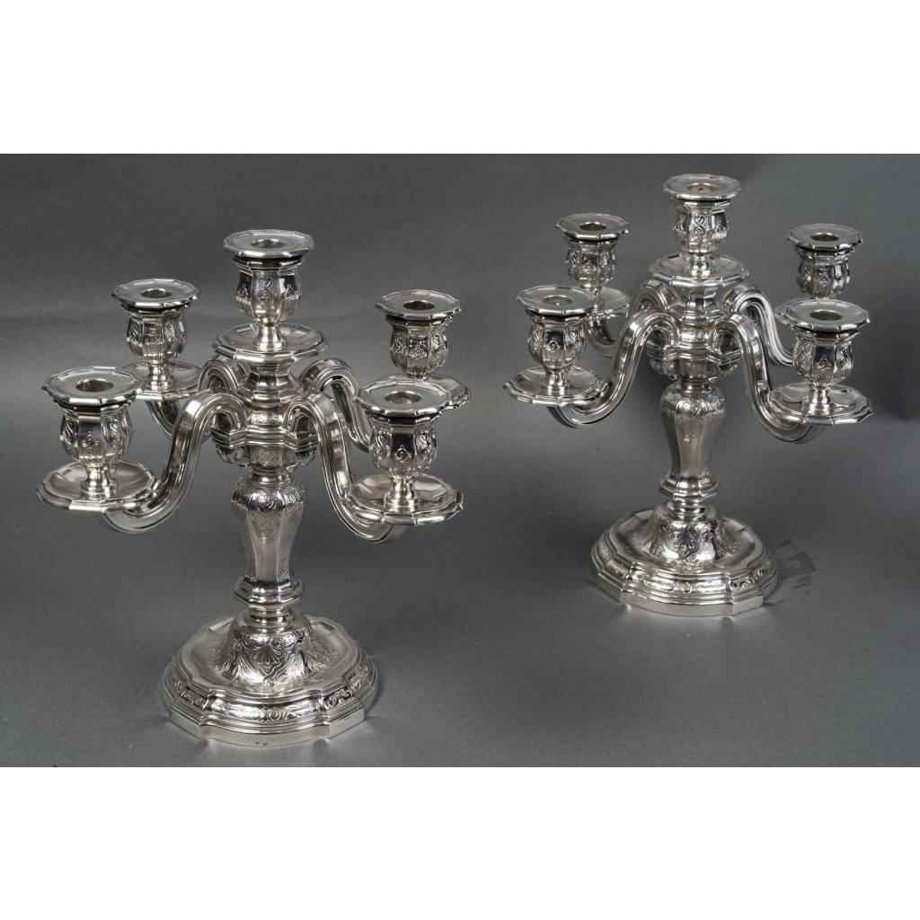 Orfèvre TETARD – Paire de Candélabres 5 lumières en argent massif XXe | Biron Orfèvre TETARD – Paire de Candélabres 5 lumières en argent massif XXe Paire de candélabres en argent massif, base ronde à doucine surmontée d’un fût à pans octogonaux supportant un bouquet à quatre bras de lumière plus une centrale. La base, le fût et les binets sont gravés et ciselés d’un décor à la Bérain dans le style «Régence ». Dimensions : Hauteur 33 cm – entraxe 35 cm Matière : Argent 1er titre 950/1°°° Poids : 4 240 grammes Poinçon : MINERVE Epoque : XXè vers 1925 Orfèvre : TETARD à PARIS Origine : France/Paris