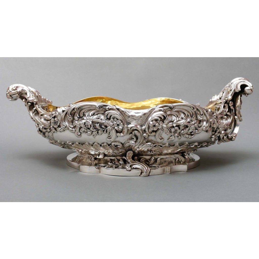 TIFFANY & Co – Importante Jardinière en argent massif époque XIXe | Biron TIFFANY & Co – Importante Jardinière en argent massif époque XIXe Importante Jardinière assymétrique en argent massif ovale, montée sur un piédouche chantourné orné de vagues d’où émerge un corps entièrement ciselé et décoré de fleurs, feuillages, rinceaux, arabesques, flanqué de chaque côté d’anses attenantes à enroulement. Doublure intérieure amovible en Vermeil. Modèle de MESSONNIER. Dimensions : Longueur : 57 cm avec anses -30 cm sans anses -Intérieur : 42 cm × 25 cm Hauteur totale : 20 cm -Base : 31 cm x 24 cm Matière : Argent 1er titre 950/°°° Poids : 7 200 grammes Poinçon : MINERVE 1 er titre Orfèvre : TIFFANY & Co PARIS Epoque : 2eme partie du XIXe siècle Vers 1853 Origine : FRANCE