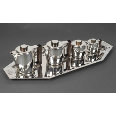 Souche-Lapparra – Service Thé/Café 4 pièces et son plateau en Argent époque ART DECO Service thé / café 4 pièces en argent massif de style moderniste, composé d’un Plateau, d’une Théière, d’une Cafetière, d’un Crémier couvert, d’un Sucrier couvert. Les corps unis sont bombés et créés une impression de fluidité tout en conservant un aspect structuré. Les couvercles circulaires sont surmontés d’une prise ronde. Prises et anses sont en palissandre. Ce service est une déclinaison d’un modèle créé par JEAN E. PUIFORCAT en 1932. Dimensions : Théière : haut 20 cm x 11 cm x 13 cm Poids : 1030 grs Cafetière : haut 19 cm x 11 cm x 15 cm - Poids : 1050 grs Crémier avec couvercle : haut 12,5 cm x 8 cm x 8,5 cm - Poids 530 grs Sucrier avec couvercle : Haut 8,5 cm - Diamètre :10 cm Poids : 390 grs Plateau : long 75 cm – larg 31,5 cm Poids : 2 Kg 847 Matière : Argent 1er titre 950/°°° Poids total : 5 Kg 847 Poinçon : MINERVE Epoque : ART DECO vers 1930 Orfèvre : SOUCHE LAPPARRA Origine : France/Paris Bibliographie et œuvre en rapport : Françoise de Bonneville – Jean Puiforcat - Éditions du regard, Paris 1986. Page 122