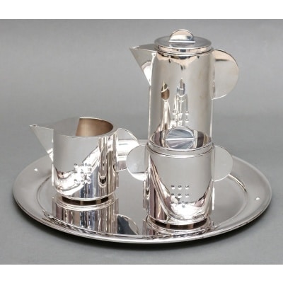 CLETO MUNARI ( 1930) Service en argent minimalisme Vicenza XXe Service en argent massif travail Italien de style minimaliste daté de 2001, comprenant un plateau rond sur lequel est posé une cafetière, un pot à lait et un sucrier, chacune des pièces est décorée de neuf petits ronds boule en repoussé sur chaque paroi latérale, les anses et prises sont des demi-cercles aplatis. Dimensions : Hauteur cafetière 17 cm – sucrier 9,5 cm – Pot à lait 7 cm Diamètre du plateau 28,5 cm Matière : Argent 1er titre 925/°°° Poids : 1159 grammes Epoque : XXe VICENZA 2001 Estampille : MUNARI sur chaque pièce Orfèvre : CLETO MUNARI ( né en 1930) Origine : Italie DU NORD