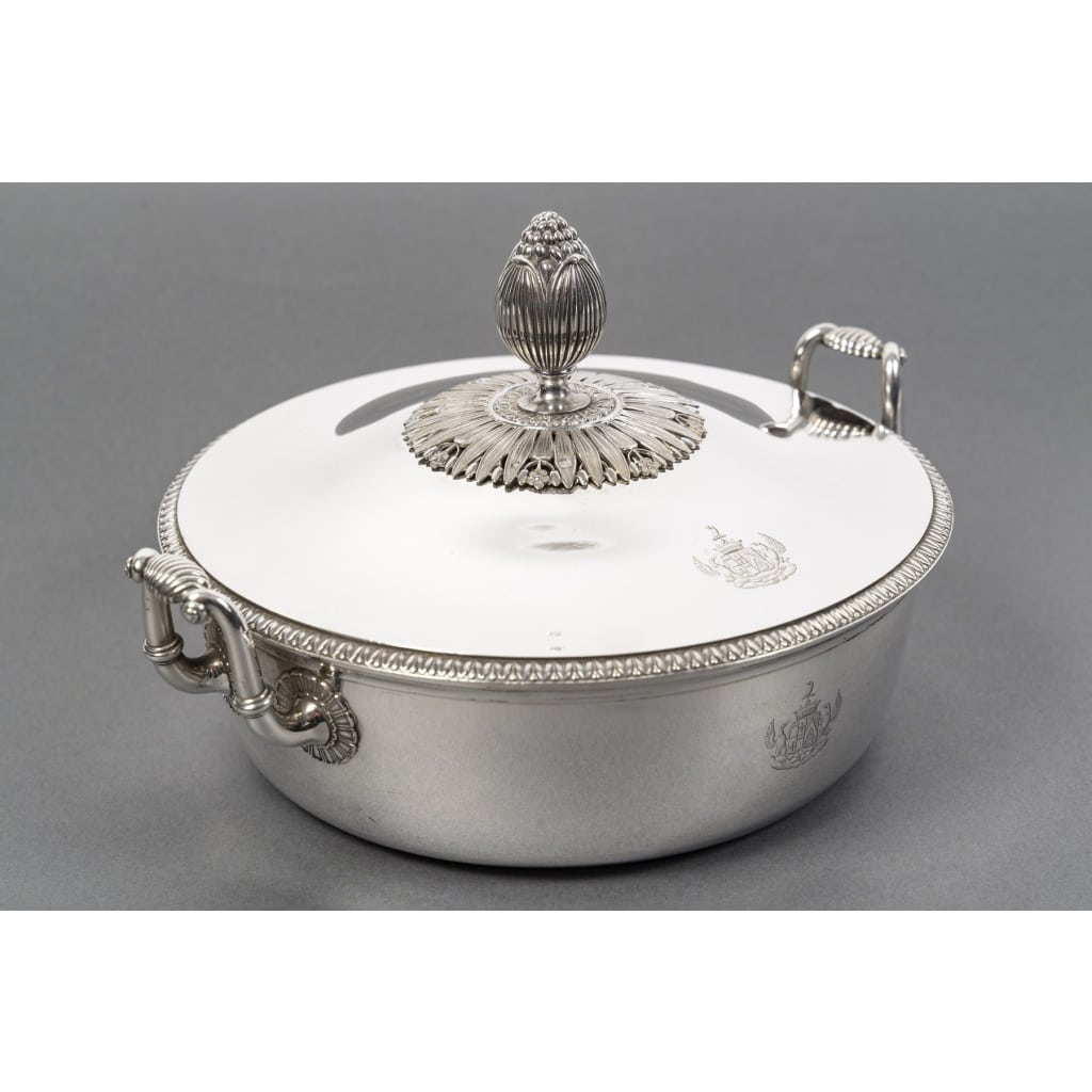 Jean Charles CAHIER – Légumier couvert en argent XIXe – 1818/1838 | Biron Jean Charles CAHIER – Légumier couvert en argent XIXe – 1818/1838 Légumier couvert en argent massif, le corps uni est doublé au col d’un liseré et flanqué de chaque côte d’anses garnies d’une demie coquille. Le couvercle est ceinturé d’une frise de palmettes et la prise est posée sur une terrasse de feuilles d’eau. Dimensions : longueur aux anses 26 cm diamètre base 18 cm hauteur 15 cm Matière : Argent 1er titre 950/°°° Poids : 1 kg 295 grammes Poinçon : Vieillard/Paris 1898- 1838 Orfèvre : JEAN CHARLES CAHIER Provenance : France/ Paris ARMOIRIES D’ALLIANCE FAMILLE « MALARTIC »