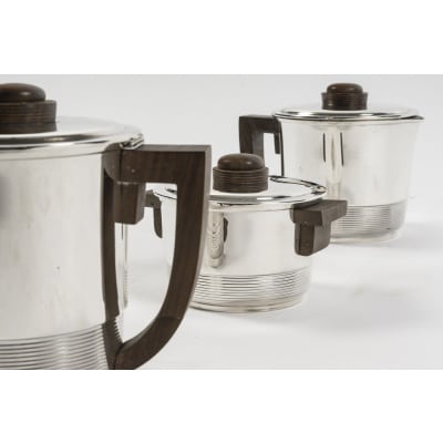 Fouquet Lapar - Service thé café 3 pièces argent massif ART DECO Service en argent massif, composé d’une Théière, d’une cafetière, et d’un sucrier couvert intérieur en vermeil, de forme cylindrique à décor fileté, couvercle à charnière pour les pots à thé et café. Les anses et prises sont en palissandre. Dimensions : Théière : Longueur : 18cm, hauteur : 14 cm Diamètre base : 10cm - Poids brut : 534 grs Cafetière : Longueur : 17cm hauteur : 16,5 cm Diamètre base 8,5 cm - Poids brut : 556 grs Sucrier : Longueur : 14,5 cm, hauteur : 9,5 cm Diamètre base : 9,5 cm - Poids brut : 364 grs Poids total brut : 1 Kg 454 Matière : argent 1er titre 950/°°° Poinçon : MINERVE Epoque : ART DECO vers 1937 Orfèvre : FOUQUET LAPAR Origine : France/Paris