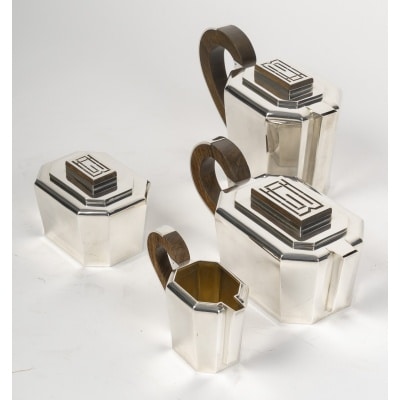 JEAN E. PUIFORCAT - Service THE/CAFE 4 pièces Argent XXe – ART DECO Service THE/CAFE 4 pièces en argent massif de forme octogonale, trapézoïdale, les anse en palissandre recouvertes d’une plaque d’argent, les prises rectangulaires sont ceinturées à la base d’argent et recouvertes d’une plaque d’argent gravée d’un monogramme dans le pur style ART DECO, d’une rare élégance. Dimensions : Théière : 24 x 11 x 11cm(haut) - Diamètre base : 13 x 9,5 cm Poids : 844 grs brut Cafetière : 23 x 10,5 x 15 cm (haut) - Diamètre base : 11 x 8,5 cm Poids : 880 grs brut Crémier : 14 x 6,5 cm - Diamètre base : 6,5 x 5,5 cm Poids : 274 grs brut Sucrier : 12,5 x 9,5 x 8 cm(haut) -Diamètre base : 11 x 8 cm Poids : 426 grs brut Poids total brut : 2 Kg 424 Matière : Argent 1er titre 950/°°° Poinçon : MINERVE Epoque : ART DECO vers 1925/1930 Orfèvre : JEAN E. PUIFORCAT Origine : France/Paris Bibliographie : Françoise de Bonneville – Jean Puiforcat – Éditions du Regard, Paris, 1986. Modèle identique reproduit page 130.