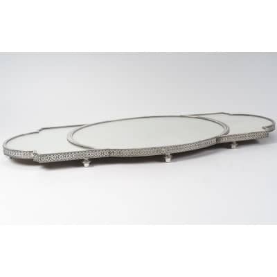 ODIOT – Surtout de table en argent 3 parties, Napoléon III, fin XIXe Important surtout de table en trois parties, à fond de miroirs sur un parquet de chêne, cernées d’une lingotière en argent massif à décor d’oves et rang de fines perles, montées sur des pieds toupies. Le centre ovale est complété par deux parties qui s’encastrent ou s’écartent selon l’usage. Dimensions : Partie centrale : 61 x 44,5 cm Longueur maxi : 107,5 cm x 44,5 cm Hauteur : 6 cm Matières : Argent 1er titre 950/1°°°, chêne, miroirs Poinçon : MINERVE Epoque : FIN XIXe Orfèvre : ODIOT/ Prévost & Cie (1895-1905) Origine : France/Paris