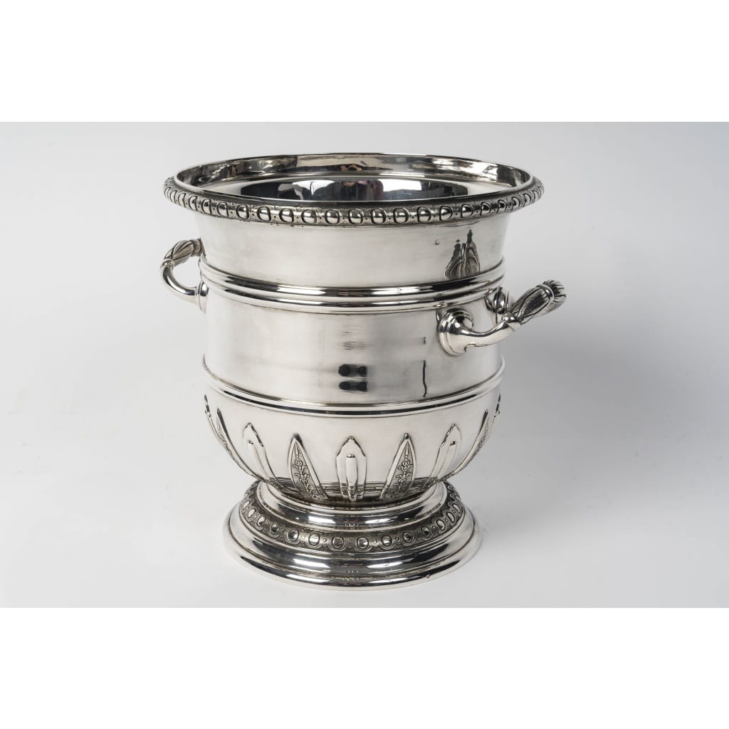 PUIFORCAT – Rafraîchissoir en argent massif de style « Régence » Fin XIXe | Biron PUIFORCAT – Rafraichissoir en argent massif de style « Régence » Fin XIXe Rafraîchissoir en argent massif monté sur un piédouche décoré haut et bas d’une frise d’oves et rangs de perles, avec motifs d’appliques à mi-corps. De chaque côté,les anses de forme demi-cylindrique, qui épousent parfaitement la courbure du récipient, assurent une prise en main stable et élégante. Leur finition lisse et épurée s’inscrit dans l’esthétique fonctionnelle et raffinée propre à la Maison Puiforcat. Dimensions : Longueur avec anses : 24 cm Diamètre au col : 20,5 cm Diamètre à la base : 16 cm Hauteur : 22 cm Matière : Argent 1er titre 950/1°°° Poids : 2 Kgs 745 Poinçon : MINERVE Epoque : FIN XIXe Orfèvre : PUIFORCAT A PARIS Origine : France/Paris
