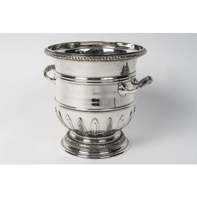 PUIFORCAT – Rafraichissoir en argent massif de style « Régence » Fin XIXe Rafraîchissoir en argent massif monté sur un piédouche décoré haut et bas d’une frise d’oves et rangs de perles, avec motifs d’appliques à mi-corps. De chaque côté,les anses de forme demi-cylindrique, qui épousent parfaitement la courbure du récipient, assurent une prise en main stable et élégante. Leur finition lisse et épurée s’inscrit dans l’esthétique fonctionnelle et raffinée propre à la Maison Puiforcat. Dimensions : Longueur avec anses : 24 cm Diamètre au col : 20,5 cm Diamètre à la base : 16 cm Hauteur : 22 cm Matière : Argent 1er titre 950/1°°° Poids : 2 Kgs 745 Poinçon : MINERVE Epoque : FIN XIXe Orfèvre : PUIFORCAT A PARIS Origine : France/Paris