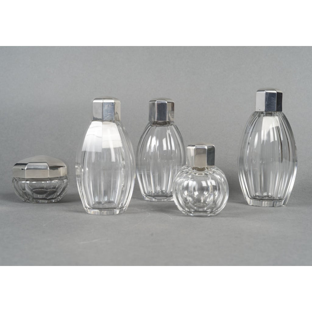 CHRISTOFLE/ BACCARAT – Ensemble de 5 flacons ART DECO circa 1930 | Biron CHRISTOFLE/ BACCARAT – Ensemble de 5 flacons ART DECO circa 1930 Ensemble de 4 flacons et un pot à onguent en cristal de Baccarat, à pans coupés, dans l’esprit du modèle Harcourt. Les flacons sont fermés avec bouchon cristal émeri, Numérotés, avec tampon gravé Baccarat 1936 /étiquette papier « entre 1925 et 1936 ». Les cols de ces 5 pièces sont sertis d’une bague en argent et couvertes d’un bouchon en argent massif à pans, signées et poinçonnées. Dimensions : 1 flacon : hauteur :15,5 cm - Diamètre : 5 cm 2e flacon : hauteur : 14,5 cm - Diamètre : 4,5 cm 3e flacon : hauteur : 14,5 cm - Diamètre : 4,5 cm 4e flacon : hauteur : 9 cm - Diamètre : 3,5 cm Pot à onguent : hauteur : 6 cm - Diamètre : 7,5 cm Matière : Cristal & argent 1er titre 950/1°°° Poids brut : 2 Kg 490 Poinçons : MINERVE & BACCARAT Epoque : ART DECO vers 1930 Orfèvre : CHRISTOFLE Origine : France/Paris