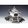 Important solid silver centerpiece represented by a covered soup tureen mounted on four scrolled feet and placed on its display stand. Rich decoration of Bérain engravings, edging of gadroons, the side handles in the form of volutes surmount mascarons, the double ogee lid has its handle in the form of a pine cone. The oval, scalloped display stand, bordered by a gadroon, has the same Bérain engraving decoration on the upright. Dimensions: Soup tureen length 39,5 cm - width 23 cm - height 28 cm Display stand: length 51 cm - width 40 cm - height 5,5 cm Total weight: 6700 grams approx. Material: 1st title silver 950/°°° Hallmark: MINERVE Period: FINISHED XIXth Goldsmith: A. AUCOC Origin: FRANCE/PARIS