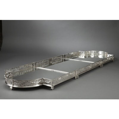 Orfèvre QUEILLE – Surtout de table en argent massif XIXè SURTOUT DE TABLE en argent massif à fond de miroir sur parquet de bois ; de forme rectangulaire, aux extrémités en demie lune, la ceinture ajourée, repercée d’arceaux, est décorée de guirlandes de lauriers retenues au centre par un médaillon armorié et, ponctuée de pilastres formant les pieds. Dimensions : longueur 152 cm – largeur 46 cm – hauteur 7,5 cm Matière : argent 1er titre 950/1°°° Poinçon : MERCURE Orfèvre : QUEILLE à PARIS Origine : France/PARIS