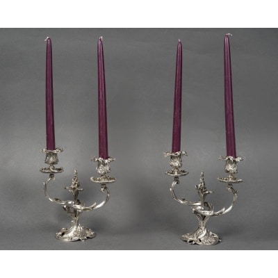 DEBAIN -Paire de bouts de table en argent massif, Louis XV époque XIXe Somptueuse paire de bouts de table en argent massif à deux bras de lumière, de style Louis XV, présentant un riche décor rocaille en relief. Chaque candélabre est composé d’un fût central torsadé à décor de coquilles et feuillages, s’épanouissant en deux bras sinueux finement moulurés, ornés de motifs végétaux naturalistes. Les binets, amovibles, sont décorés de larges feuilles nervurées et reposent sur des bobèches ourlées de volutes et de feuillages en chute. La base circulaire mouvementée adopte la forme d’un cartouche animé de ressauts, godrons et agrafes feuillagées. Dimensions (chaque pièce) : Hauteur : 20 cm - Largeur : 22,5 cm Diamètre de la base : 10 cm Poinçon : Minerve 1er titre 950/1000 Poids total : 2 Kgs 140 Epoque : fin du XIXe siècle. Orfèvre : François-Alphonse Debain (Paris, actif de 1864 à 1894) Poinçon de maître F.A.D pour François-Alphonse Debain, insculpé en 1864 au 79 rue du Temple à Paris. Origine : France/Paris