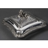 CARDEILHAC - LÉGUMIER COUVERT EN ARGENT MASSIF XIXe Légumier carré à angles adoucis de style Louis XV, orné d’une frise de coquilles et de guirlandes feuillagées finement ciselées. Le couvercle à côtes torsadées est sommé d’une prise en forme de bouquet de fleurs et feuillages naturalistes. Monogramme gravé sur la panse. Dimensions : 24 × 24 cm - Base : 17,5 × 17,5 cm - Hauteur : 13 cm Matière : Argent 1er titre 950/1°°° Poids brut : 1 490 g Poinçon : MINERVE Epoque : FIN XIXe Orfèvre : CARDEILHAC A PARIS Origine : FRANCE/PARIS Bibliographie : Maison Cardeilhac (1804-1951) Fondée en 1804 par Antoine-Vital Cardeilhac, la maison Cardeilhac s’est rapidement imposée parmi les orfèvres parisiens les plus prestigieux du XIXᵉ siècle. Réputée pour la qualité de ses ciselures et ses créations à la fois classiques et novatrices, elle excelle particulièrement dans la réinterprétation des styles Louis XV et Rocaille, prisés sous le Second Empire et la Troisième République. Sous la direction successive de ses descendants, Cardeilhac participe aux grandes Expositions Universelles de Paris (notamment 1867, 1878, 1889 et 1900) où elle obtient plusieurs médailles et distinctions. Elle développe des services de table raffinés, des pièces de prestige et des orfèvreries d’exception, souvent commandées par une clientèle aristocratique et bourgeoise. En 1951, la maison Cardeilhac est rachetée par Christofle, qui perpétue une partie de ses modèles et conserve l’héritage de son savoir-faire. Aujourd’hui, les pièces signées Cardeilhac sont très recherchées pour leur élégance et leur qualité de fabrication, illustrant l’âge d’or de l’orfèvrerie française.