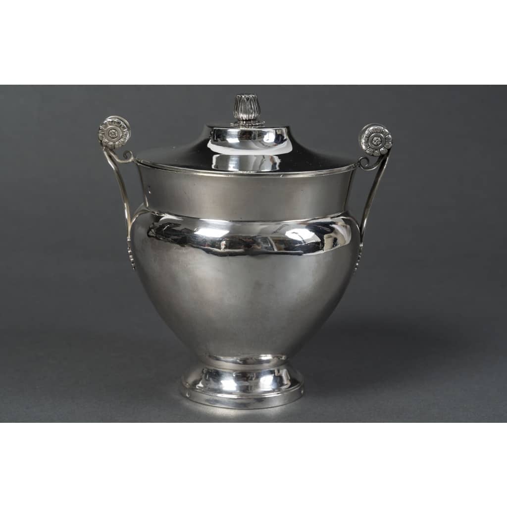 JBC ODIOT – Sucrier couvert en argent époque 1er empire 1809/1818 Élégant sucrier couvert de forme ovoïde en argent massif, reposant sur un piédouche circulaire, avec couvercle bombé orné d’une prise stylisée en graine. Les anses latérales, finement ciselées de palmettes et de rosaces sur fond amati, témoignent d’un répertoire décoratif typique du goût néo-pompéien sous l’Empire. Pièce éxécutée entièrement au marteau. Le poinçon de garantie au 2e coq atteste d’une fabrication entre 1809 et 1818. Cette œuvre est signée Jean-Baptiste Claude Odiot, l’un des plus prestigieux orfèvres parisiens du Premier Empire, célèbre fournisseur de la Cour impériale et de nombreuses cours européennes. Il succède à son père et fait rayonner l’orfèvrerie française à travers des créations alliant rigueur architecturale et richesse ornementale, souvent inspirées de l’Antiquité. Dimensions : H. 14 cm – L. avec anses : 13,5 cm – Diam. base : 6 cm Matière : Argent 1er titre 950/1°°° Poids : 370 grammes Poinçons : SUR LA BASE 2eme COQ 1809/1818 PARIS– Récence du 2eme Coq – Poinçon du vieillard 1818/1838 avec recense du sanglier. SUR LE CORPS : 2eme COQ 1809/1818 PARIS– Récence du 2eme Coq – Poinçon du vieillard 1818/1838 avec recense du sanglier. SUR LE COUVERCLE : 2eme COQ 1809/1818 PARIS– Récence du 2eme Coq – Poinçon du vieillard 1818/1838 avec recense de la garantie SUR LE CORPS ET LE COUVERCLE : Poinçon en losange de JEAN BAPTISTE CLAUDE ODIOT Orfèvre : Jean-Baptiste Claude Odiot (Paris, 1763–1850) Origine : France/Paris